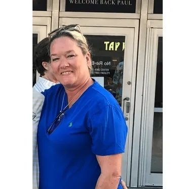 Person wearing a blue shirt standing in front of a building entrance with a welcome sign.
